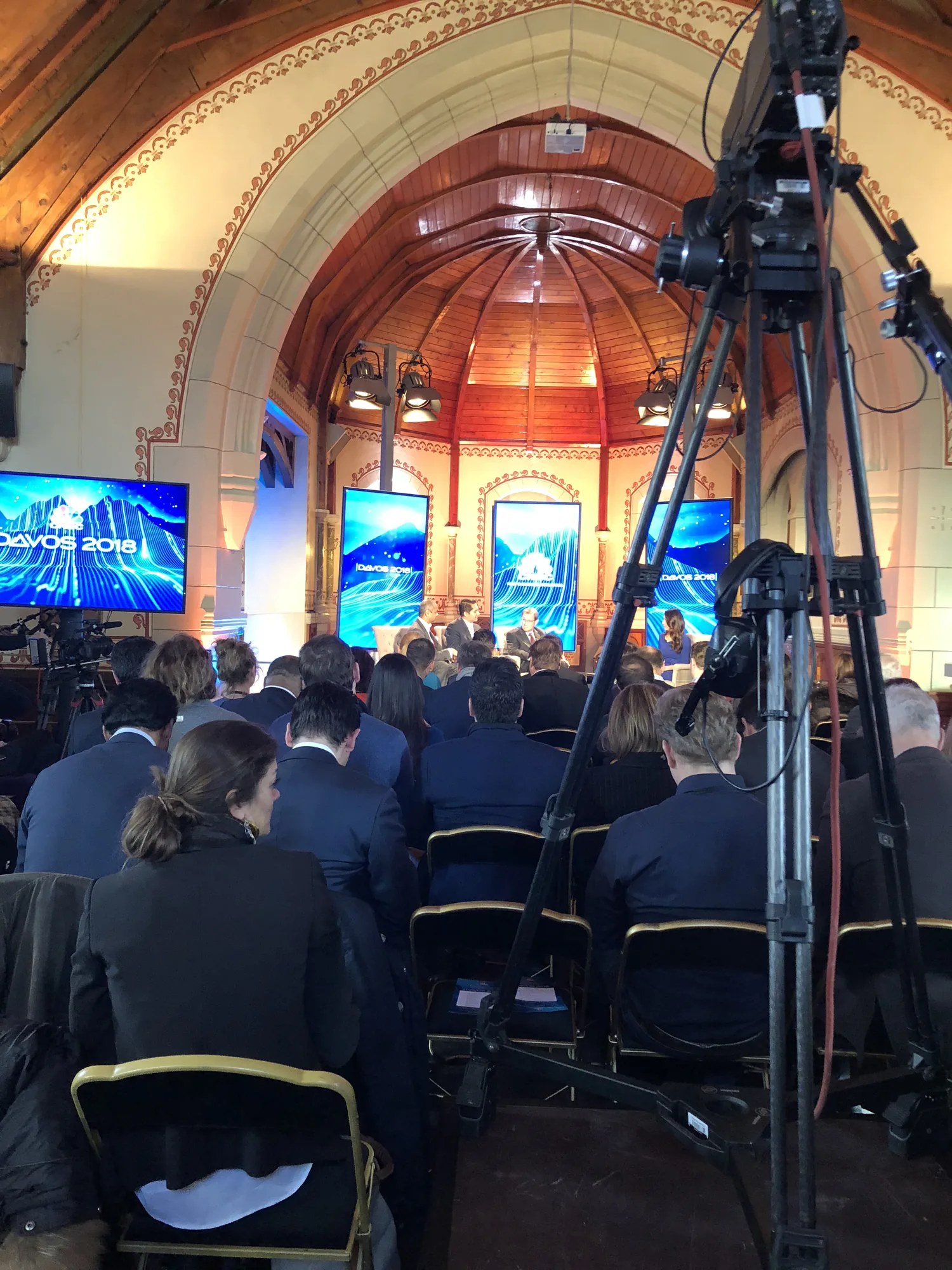 A packed broadcast studio inside a converted Davos hall, camera crew and audience together during a panel