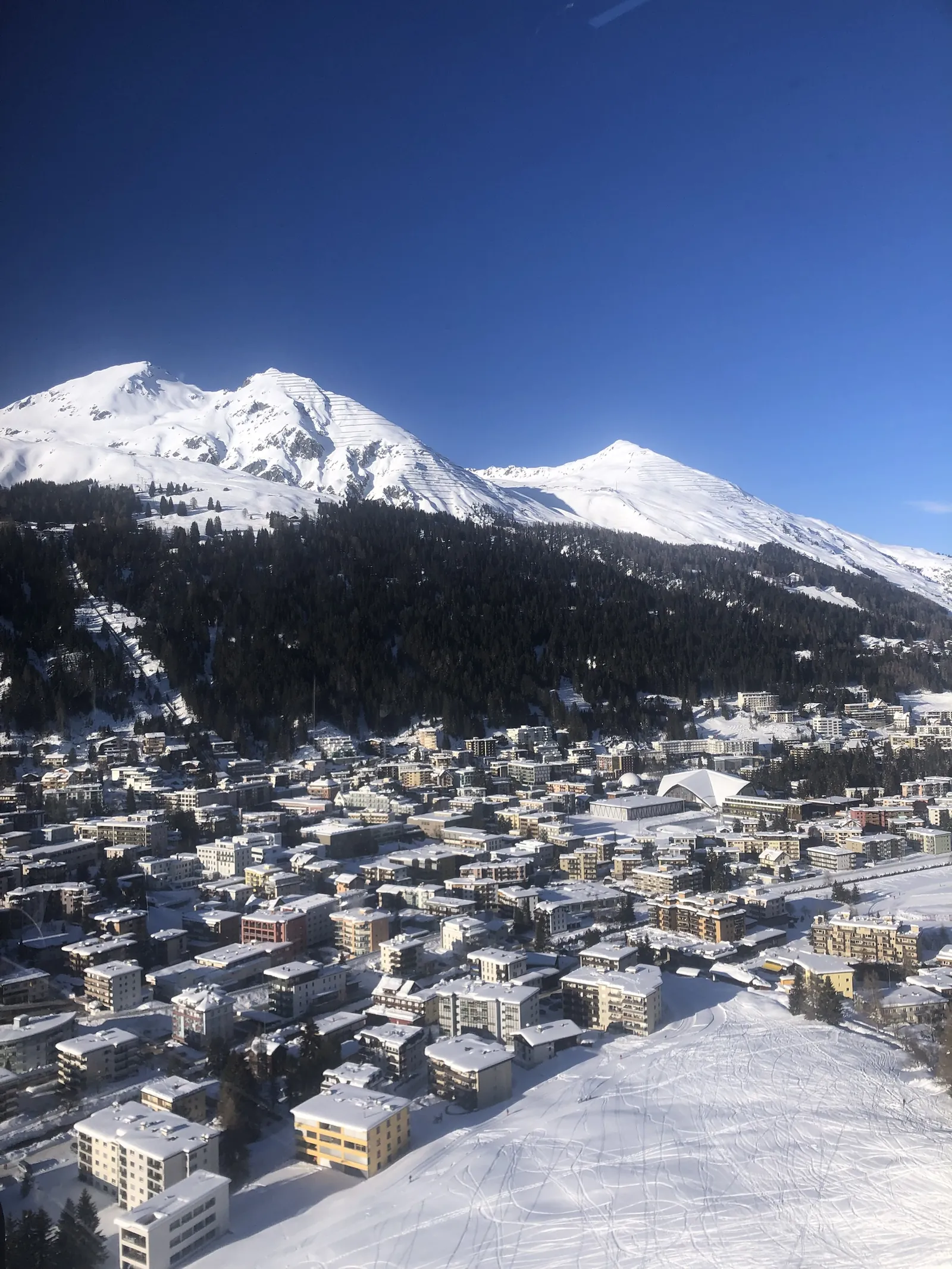 Davos from above on a clear January day, snow on every roof and the ice stadium in the middle of town